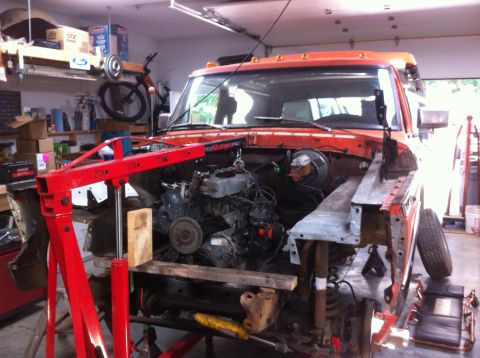 1978 Ford Bronco - An orange truck is in a garage, with its engine removed and supported by an engine hoist.