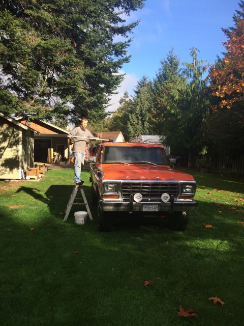 1978 Ford Bronco - A man washes an orange Ford pickup truck in a grassy yard on a sunny day.