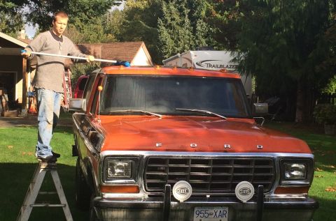 1978 Ford Bronco - A man washes an orange Ford truck from a ladder in a driveway.