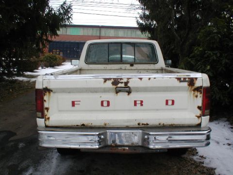 1986 Ford F-150 - The rear of a white Ford pickup truck shows significant rust damage around the tailgate and taillights.