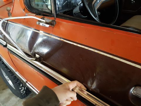 1978 Ford Bronco - A hand reaches for the chrome trim on a damaged two-tone door of an older vehicle.