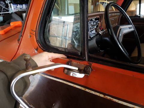 1978 Ford Bronco - The interior of an orange and brown 1978 Ford Bronco shows a hand reaching for the door handle.