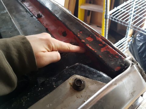 1978 Ford Bronco - Close-up of a hand pointing at a corroded metal section, possibly under a hood.