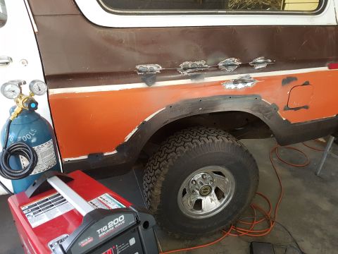 1978 Ford Bronco - Welding equipment sits next to a Ford Bronco undergoing body repair, showing areas of rust and fresh welds.