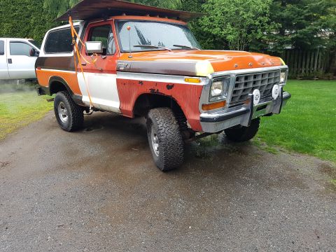 1978 Ford Bronco - This 1978 Ford Bronco is parked on a gravel driveway next to a white pickup truck, with a wooded area in the background.