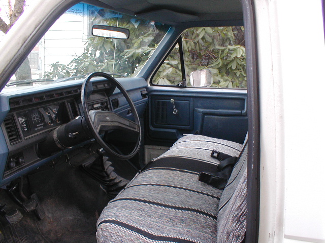 Interior shot of a truck cab showing the dashboard, steering wheel, and bench seat with a striped cover