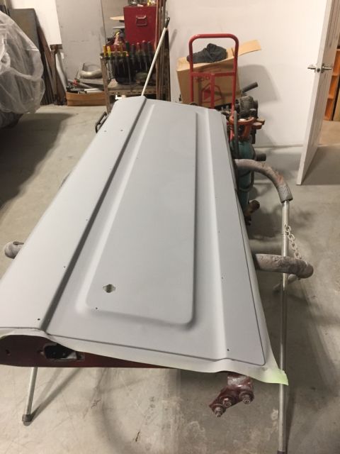 1978 Ford Bronco - A vehicle hood, prepped with primer, rests on a stand in a workshop setting.