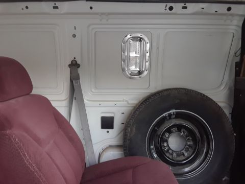 1999 Ford E250 - The interior of a van shows a maroon seat, a spare tire, and a light fixture on the wall.