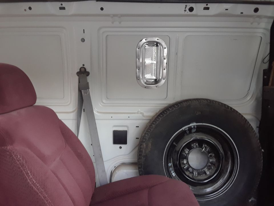 Van interior cargo area with maroon seat, spare tire, and a light fixture on the wall