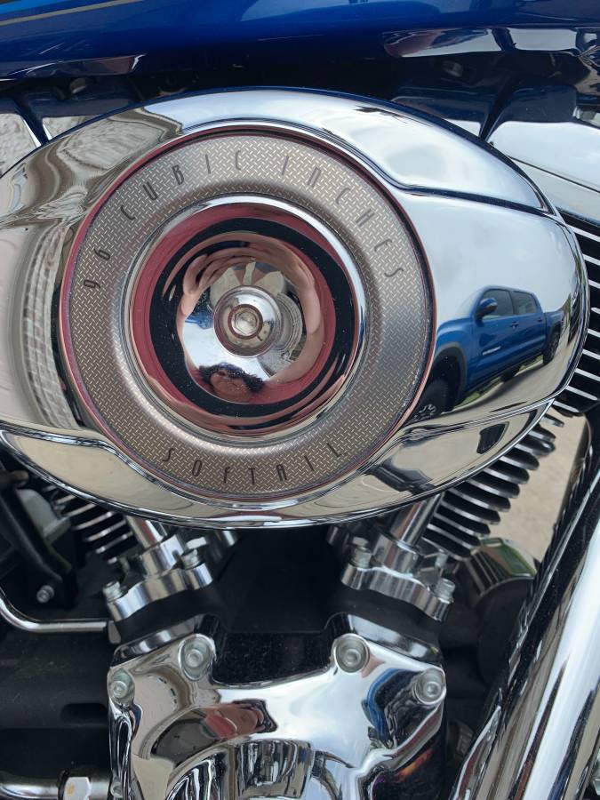 Chrome air cleaner cover with '96 CUBIC INCHES SOFTAIL' text, reflecting a blue pickup truck