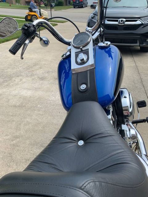 2008 Harley-Davidson Softail - A blue motorcycle is parked on a driveway, with a person on a riding lawnmower in the background.
