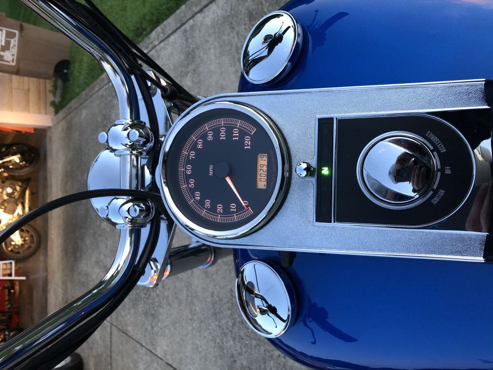 Blue motorcycle dashboard with chrome handlebars, speedometer, and ignition switch. Odometer reads 002919