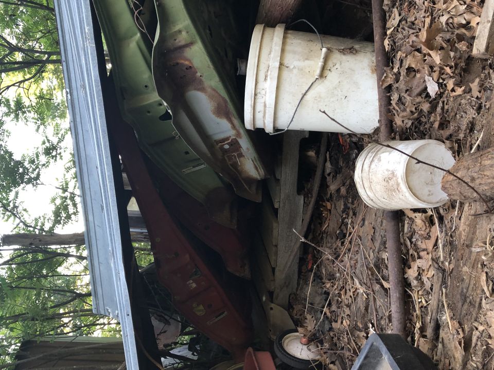rusted car body panels and two white buckets in a cluttered outdoor area