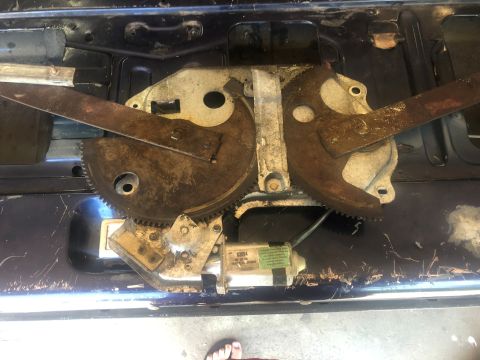 1995 Ford Bronco - Close-up of a rusty tailgate window regulator mechanism, likely needing repair or replacement.
