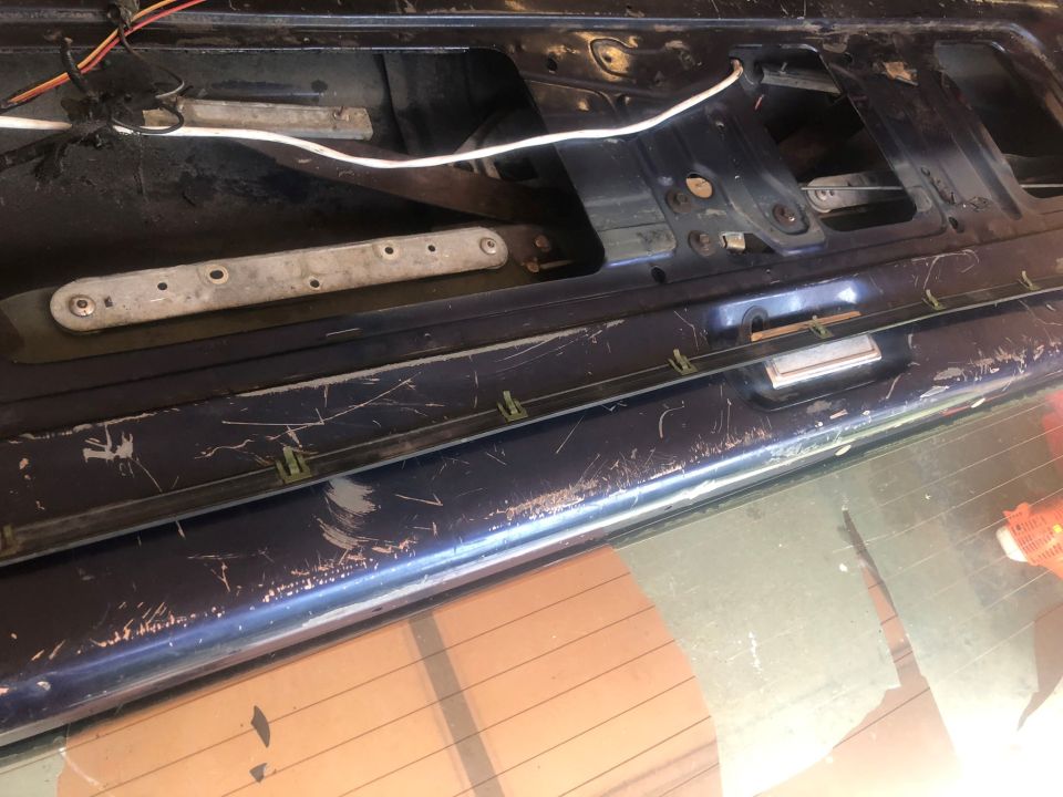 Dark blue car tailgate interior with visible scratches and wiring. A metal bracket is mounted horizontally