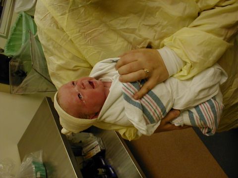 1983 Ford Bronco - A newborn baby, swaddled in a blanket, is held by adult hands in what appears to be a medical setting.