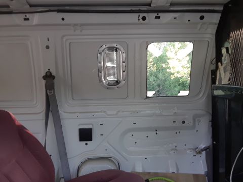 1999 Ford E250 - The interior of a white cargo van shows a seat, seatbelt, and a window with trees visible outside.