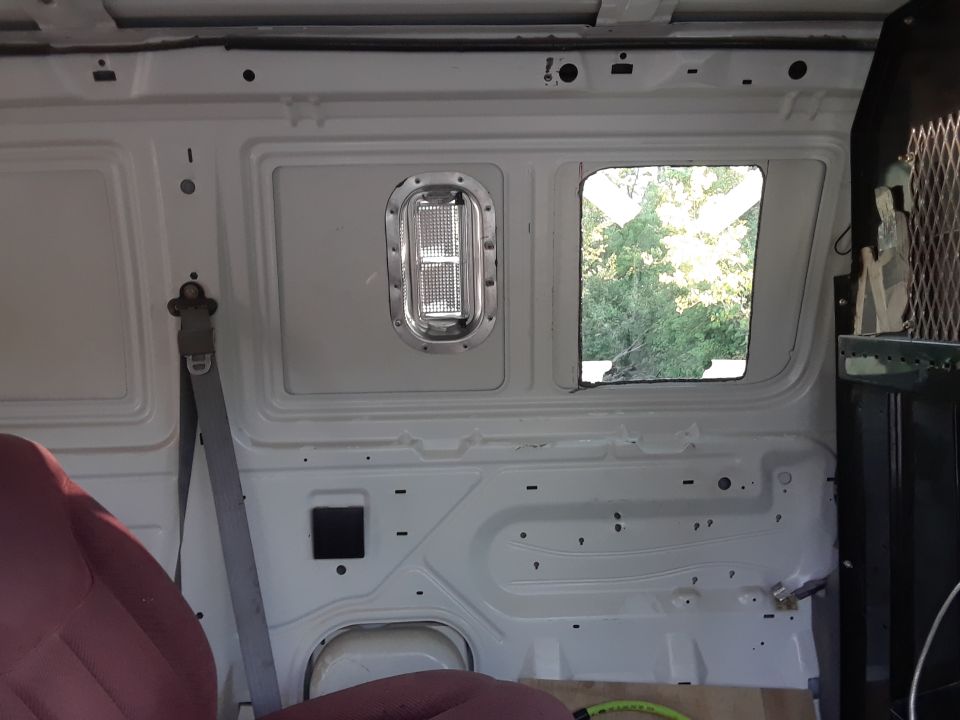 White van interior cargo area with maroon seat, gray seatbelt, and a window showing trees