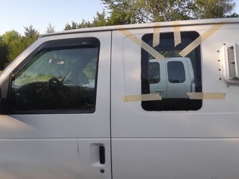 1999 Ford E250 - A white cargo van is seen from the side, with a window covered in tape. Another white van is visible in the reflection.