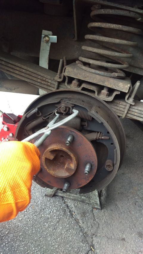 1988 Ford Bronco - A mechanic works on a vehicle's brake drum assembly, showing the internal components and suspension.