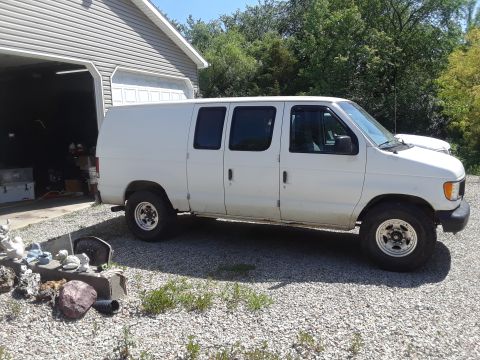 1999 Ford E250 - A white cargo van is parked in front of a garage on a sunny day.