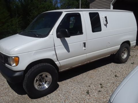 1999 Ford E250 - Side view of a white van with a dent on the front fender and aftermarket wheels.