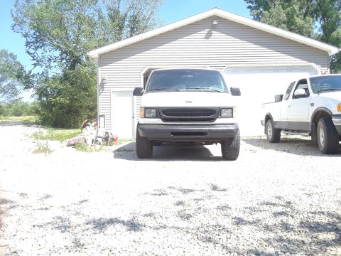 1999 Ford E250 - A white 1999 Ford E250 van is parked in front of a garage, with a pickup truck to its right.