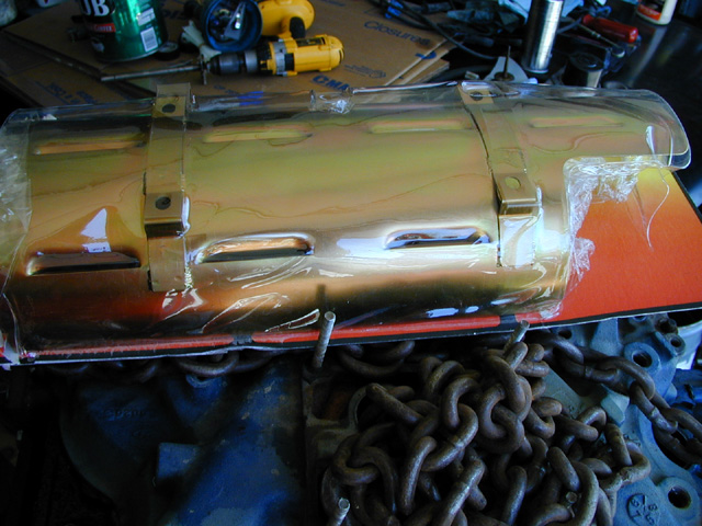 Engine part covered in plastic wrap, with heavy chains in the foreground