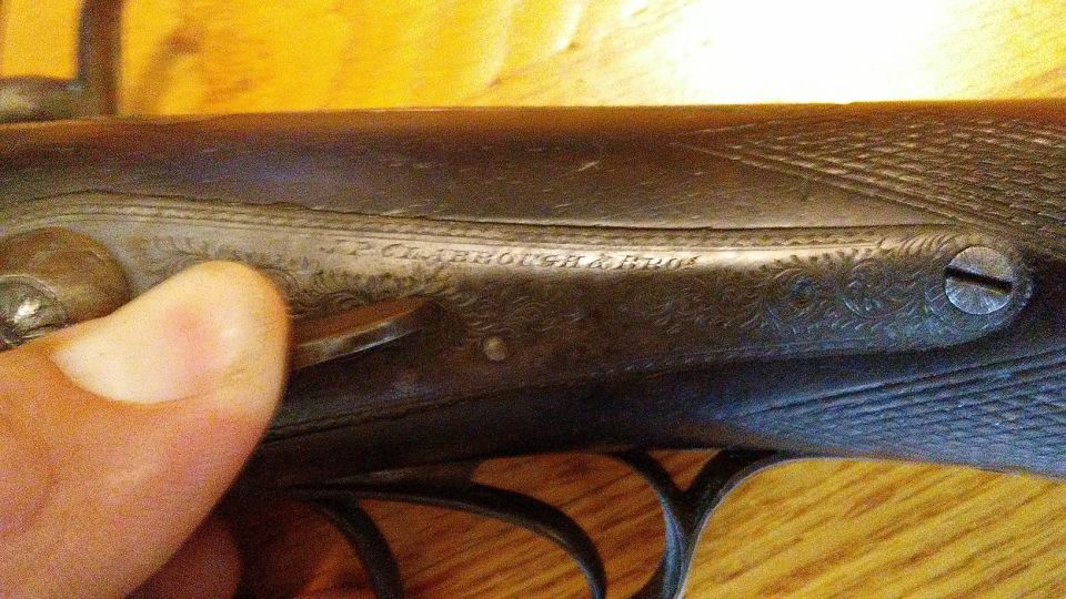 Close-up of engraved text on a dark metal firearm part, with a thumb visible