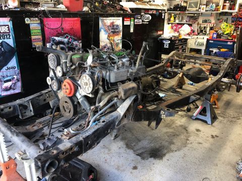 1992 Jeep Wrangler - The chassis and engine of a Jeep are disassembled and supported by jack stands in a workshop.