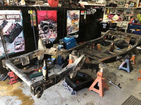 1992 Jeep Wrangler - The bare frame of a vehicle is supported by jack stands in a cluttered garage setting.