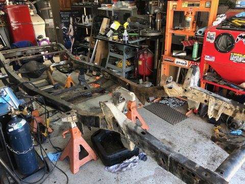 1992 Jeep Wrangler - The frame of a vehicle is disassembled and supported by jack stands in a workshop environment.