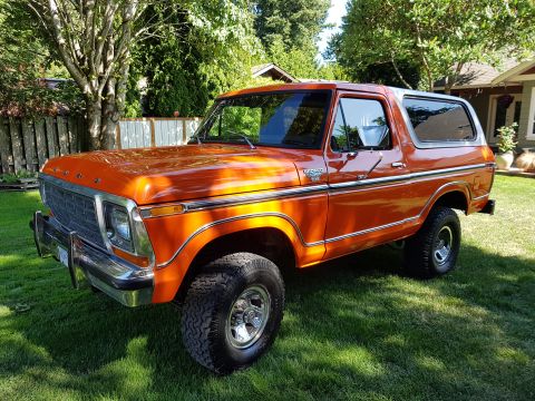1978 Ford Bronco - This orange Ford Bronco is parked on a grassy lawn with trees and a house in the background.