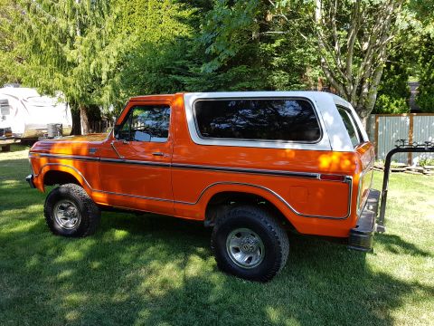 1978 Ford Bronco - This orange 1978 Ford Bronco with a white hardtop is parked on a grassy lawn with trees in the background.