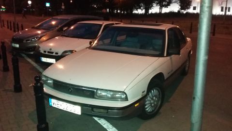 White sedan parked at night, front view. License plate visible
