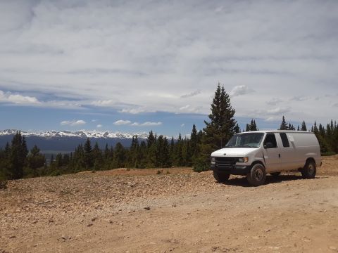 1999 Ford E250 - A white cargo van is parked on a gravel road overlooking a valley and snow-capped mountains.
