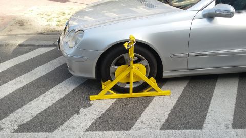 Silver car with yellow wheel clamp on crosswalk