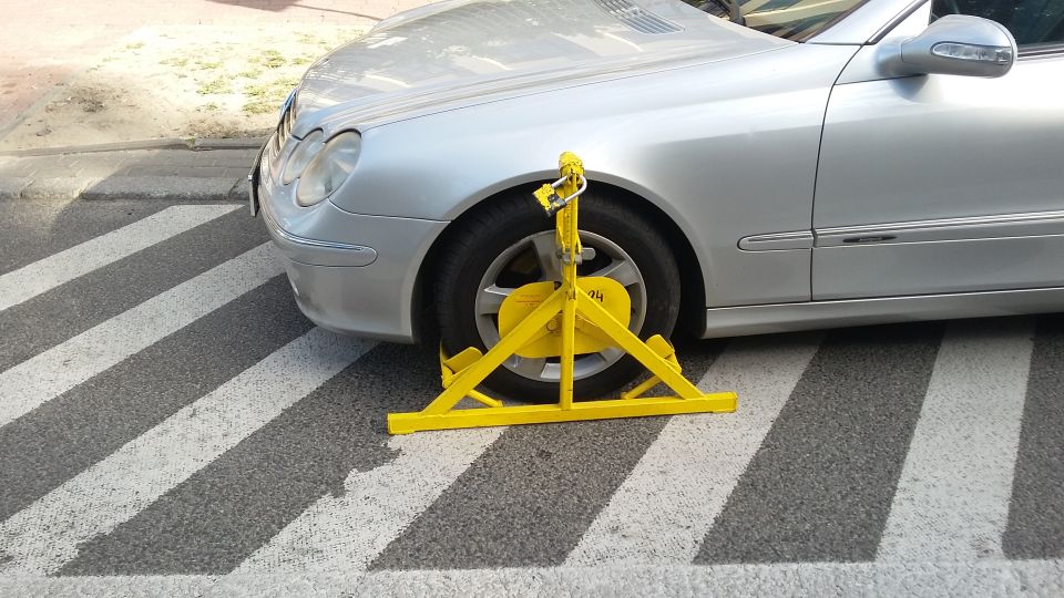 Silver car with yellow wheel clamp on crosswalk
