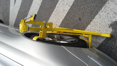 Silver car's front wheel secured by a yellow clamp