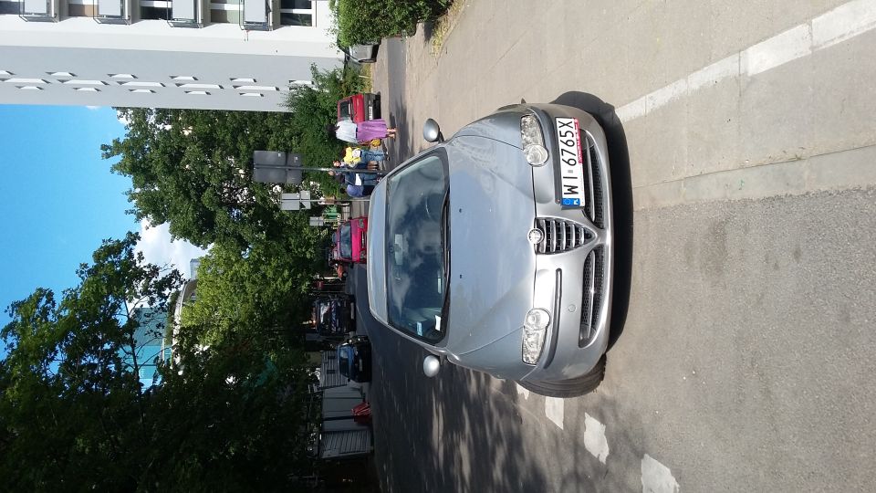 Silver sedan parked on street, front view. License plate WI-6765X. Other cars and building in background