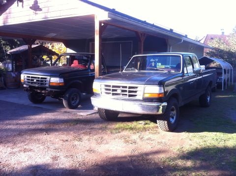 1978 Ford Bronco - Two Ford F-Series trucks are parked side-by-side under a covered carport.