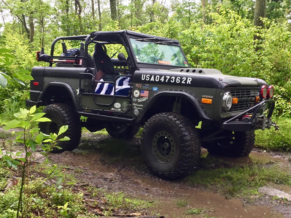 1972 Ford Bronco with USA047362R painted on hood, parked on a dirt trail in woods