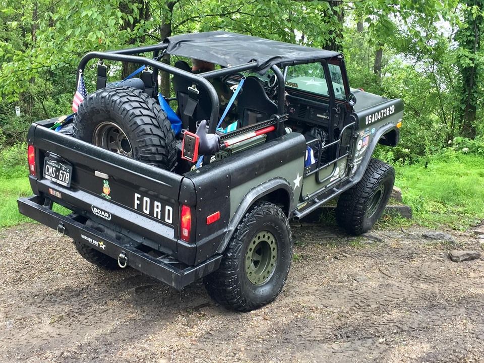 Black and olive green 1972 Ford Bronco with roll cage and spare tire in bed