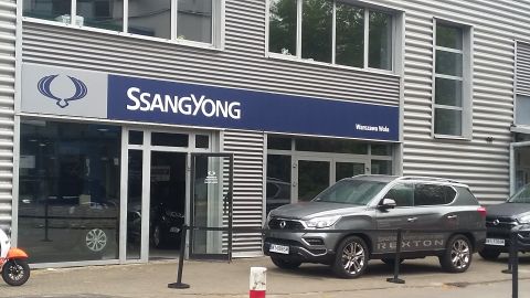 Gray SsangYong Rexton SUV parked in front of a dealership, showing "Rexton" text on the door