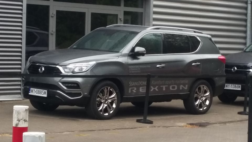 Gray SsangYong Rexton parked outside a building, with another vehicle visible to the right