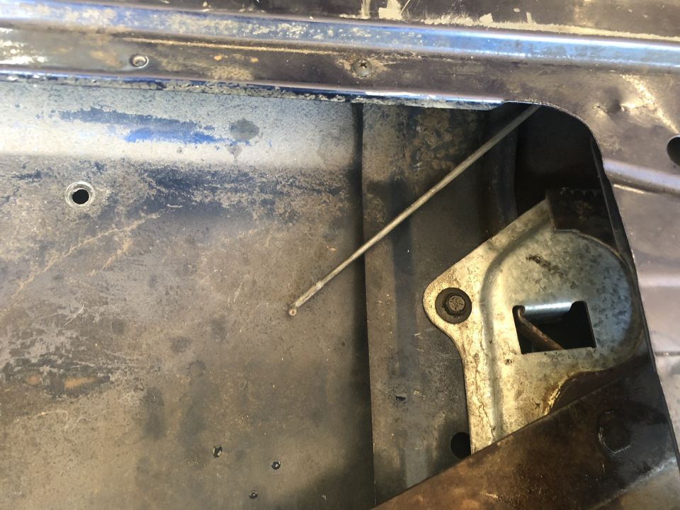 Tailgate latch mechanism with a thin metal cable extending diagonally. The metal shows signs of wear and dirt