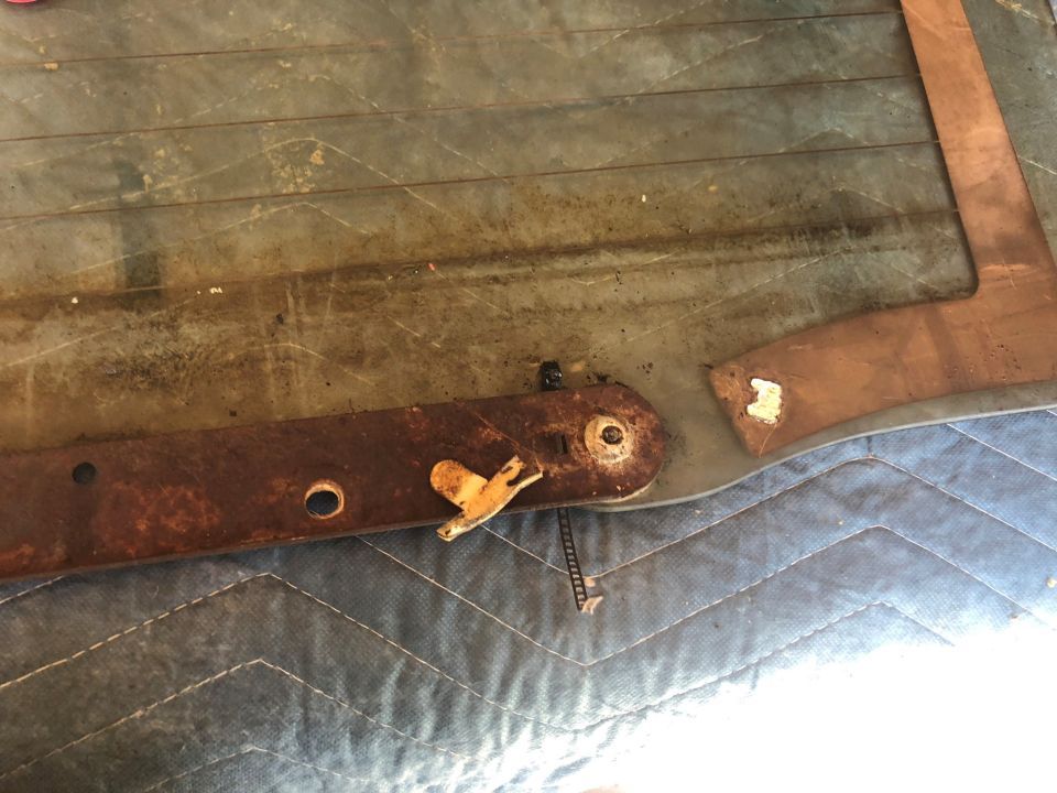 Rusty tailgate latch mechanism with yellow lever and chain, on a blue quilted surface