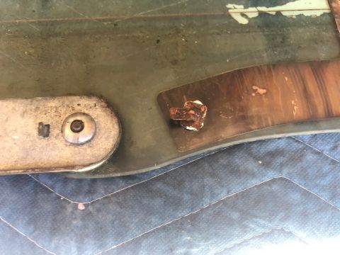 1995 Ford Bronco - A close-up view shows a rusted bolt and bracket attached to a green panel, with a wood-grain pattern visible underneath.