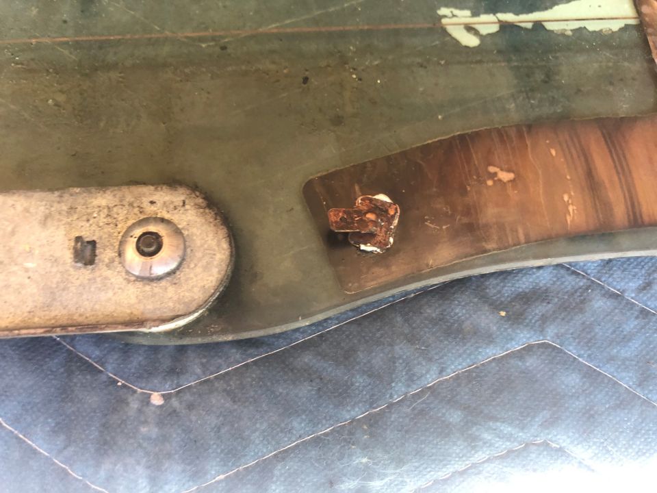 close-up of rusted bolt and bracket on a green panel, possibly from a car part