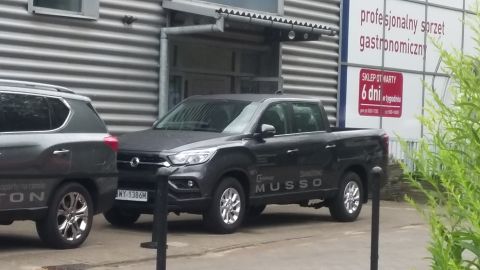 Dark gray SsangYong Musso pickup truck parked next to a dark gray SUV, front 3/4 view